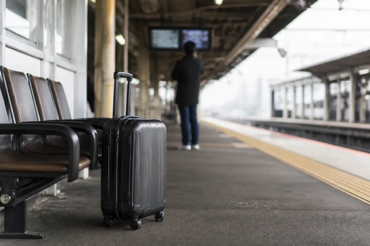 A suitcase waits beside a Japanese train platform while a traveler checks the departure area